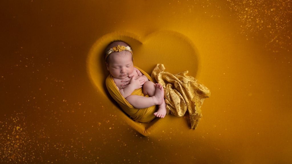 Baby girl posed on heart shape with gold background