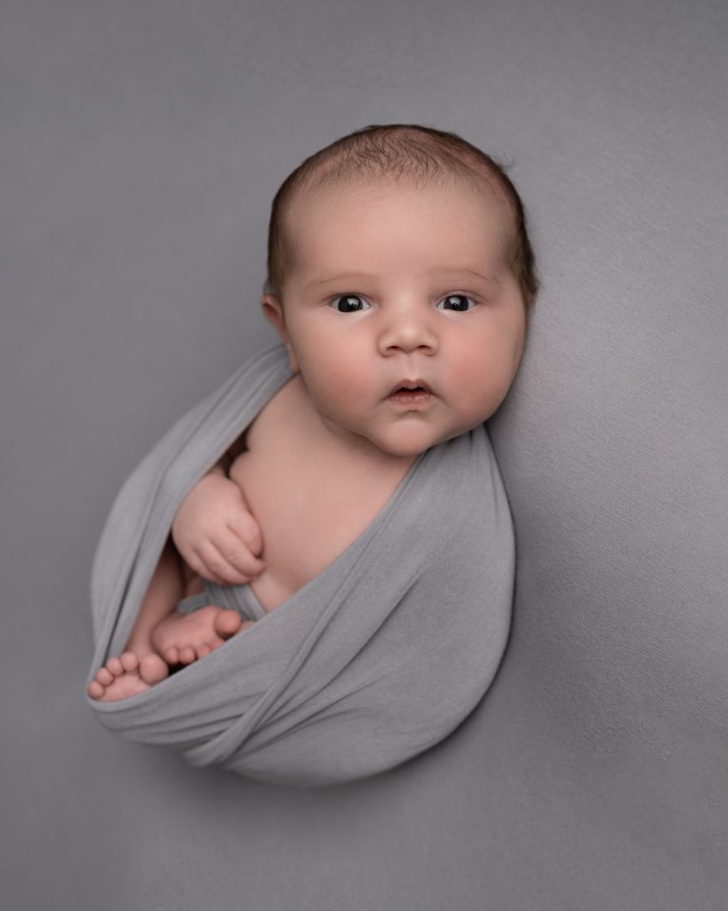 newborn baby boy wide awake dressed in grey wrap