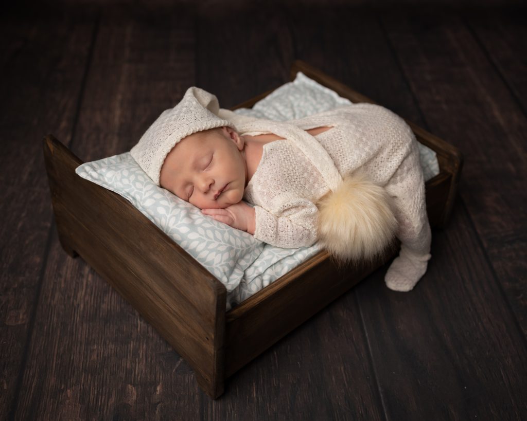Baby boy posed on a little wooden bed